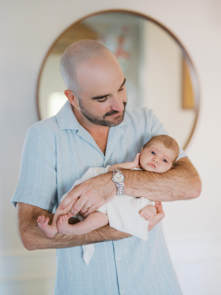 dad holds newborn baby while baby looks out during in home lifestyle newborn photos in fort worth
