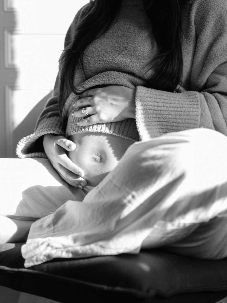 maternity photography in DFW, mom holds baby bump with light shining through, image is in black and white