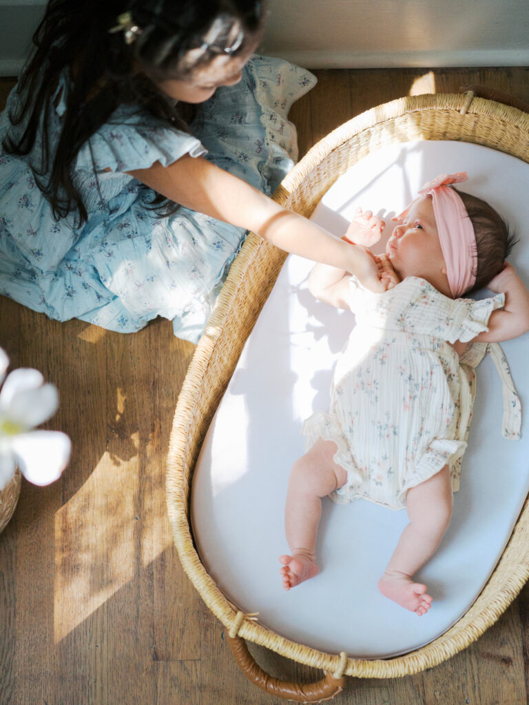 sister touches newborn sister in sunlight during newborn photos