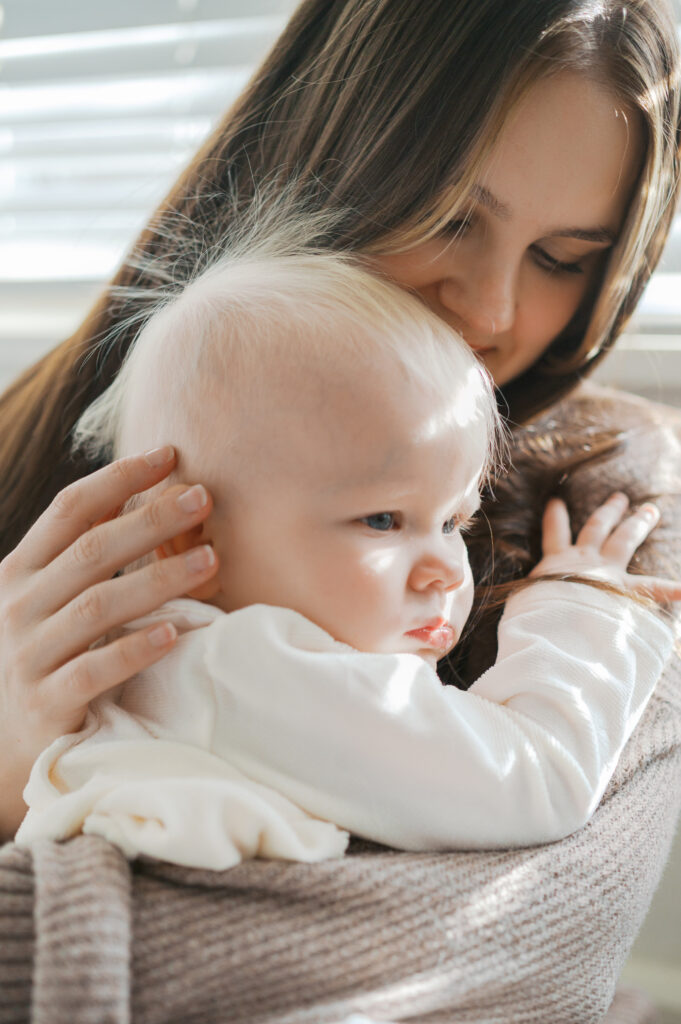mom holds baby close next to window as light pours in