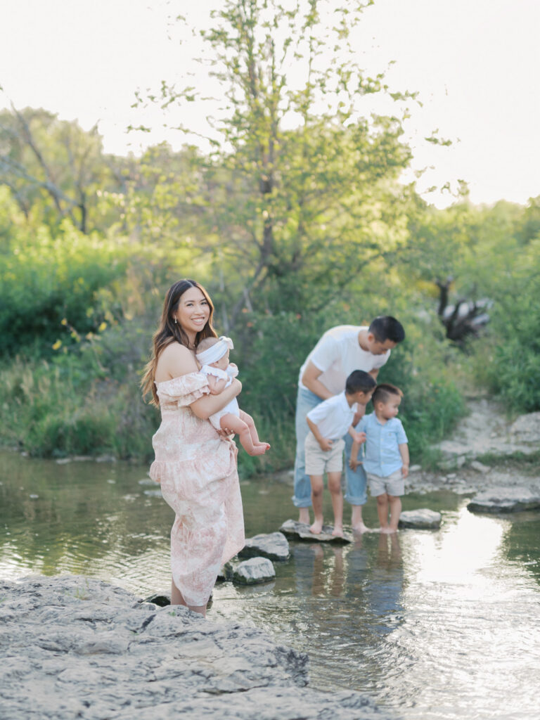 a family splashes in a fort worth creek and mom looks back at camera during spring family photos